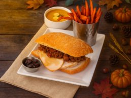 Combo 2 de Thanksgiving en TGI Fridays Tijuana: Sándwich de pavo con relleno, papas de camote fritas y crema de calabaza servido en un plato blanco.
