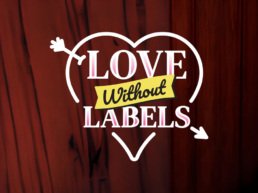 Logotipo oficial de la campaña Love Without Labels de San Valentín en Fridays Tijuana. Corazón blanco con flecha y cinta amarilla sobre fondo de madera roja.