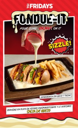 Mano vertiendo salsa de queso caliente sobre una hamburguesa con queso, tocino y papas fritas en un plato de hierro chisporroteante en TGI Fridays Tijuana.